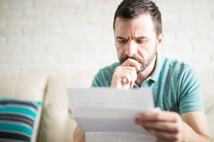 Close up shot of a young adult man reading the mail in the living room and worried about his credit card payments